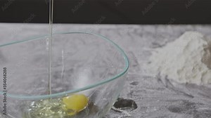 Woman's hand breaking an egg into a glass bowl on a table with flour. Slow motion, Full HD video, 240fps, 1080p. Step by step homemade dough preparation.