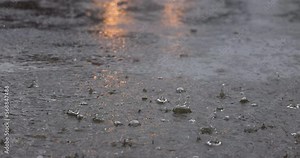 Raining in slow motion of raindrop hit the dirty wet cement road with light from car headlight reflect on water on the background.