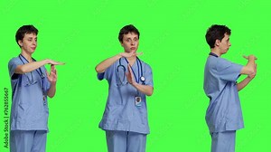 Medical assistant giving timeout symbol against greenscreen backdrop, showing limits and asking for a break. Nurse doing pause or stop gesture while she wears blue scrubs. Camera B.