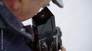 elderly man is filming by old video camera, looking into lens and rotating handle, close-up view