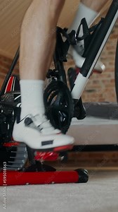 A man pedals a bicycle standing at a holding station, close-up of male legs, no face. Indoor cycling in a stylish home interior