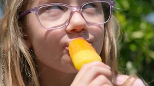 Close-up video portrait of a child girl eating ice cream. The child enjoys colored frozen juice or popsicle. Summer lifestyle video.