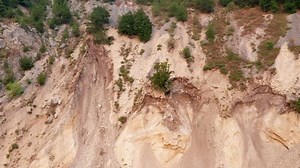 Soil erosion on a steep slope due to landslide. Surface ground movement on unstable hillside. Coastal land deterioration and collapse. Aerial drone view.