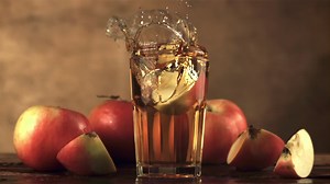 Super slow motion in a glass with apple juice falls a piece of apple with spray. On a brown background.Filmed on a high-speed camera at 1000 fps.