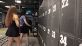Two women standing by numbered gym lockers, organizing their...