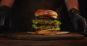 Chef making burger on serving board.