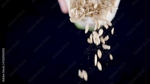 Oat flakes falling and scattering from white measuring package on black background, organic healthy breakfast cereals in slow motion macro video with floating particles