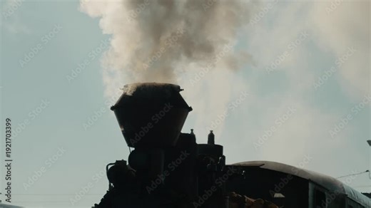 Mocanita steam train stands at the station in Bucovina, Romania, releasing white smoke into the air as it awaits departure. This old locomotive is a sight to see.