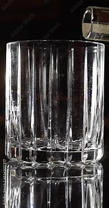 vertical social media high resolution close up of whiskey or bourbon being poured into a glass on a bar with an ice splash at the end
