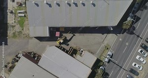 Suburban traffic moving past active mobile crane moving heavy metal beam to and from factory floor.