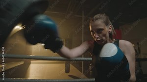 Medium shot of female battler wearing gloves training before competition and doing jabs at boxing gym