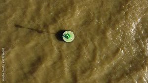 Aerial top view showing Green buoy floating on brown water of Paraná River at sunset