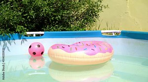 Children swimming pool, pink ball and donut float on sunny summer day. Inflatable pool toy donut in swimming pool on the garden.