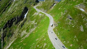 Swiss yellow bus driving on serpentine towards a hotel with lake at grimselpass, while camera slowly follows its movement with other cars on the road.