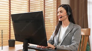 Female call center operator or customer service helpdesk staff working on workspace while talking on the headset to provide assistance for customer. Professional modern business service. Blithe
