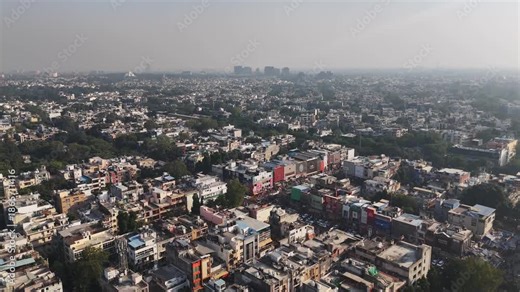 Wide aerial view of Delhi city with dense housing clusters, tree-lined areas, and a sprawling metropolitan horizon.