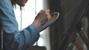 A palette for mixing paints. Artist's tools: artist holds a palette for mixing paints and types paint with a brush. Artist dabs brush in a palette with paints and applies a smear on canvas.