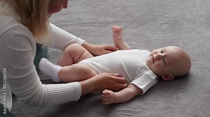 Baby lies on bed after waking up, mother tickles the infanta heel. Mom shows love and care by playing with newborn baby, tickling him. Concept of mother love, care, infancy, maternity leave.