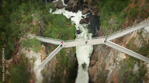 Bird's eye view of the new viewing platform at the Voringfoseen waterfall. An intricate metal structure hanging above the deep ravine. People standing on a platform admiring the view. Tilt-shift.