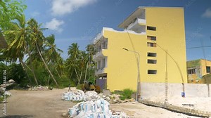 Real estate development erodes lush exotic greenery on island of Himmafushi. Palm trees rustle next to a row of tourist apartment building under construction on a remote exotic island in the Maldives.