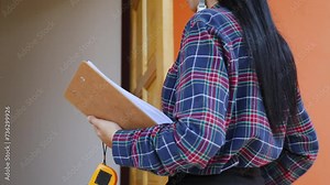 Asian house's construction inspector female in hard hat reviews architectural plans examining integrity building's interior, clipboard and measuring tape in hand, ensuring compliance safety standards