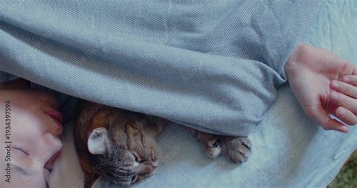 60 fps 4k dolly shot of a teenage girl and her cat resting quietly together in bed, wrapped in warmth and comfort as they enjoy a peaceful sleep.
