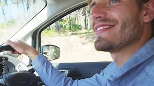 Young smiling man driving a car on a road trip
