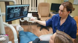 Dentist talking, gesturing and showing results of x-ray teeth on monitor screen to patient in dental chair. Cabinet in tooth clinic. Preventive examination. Treatment, healthcare and medicine.