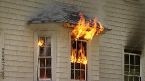 House window burning in fire as flames shoot out of the window and burn the wall