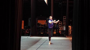 Male ballet dancer stretching backstage under dramatic stage lighting