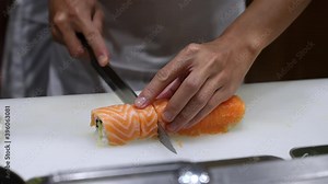 4K Professional chef using kitchen knife slice salmon with shrimp tempura sushi roll on kitchen counter. Male chef preparing food healthy food menu rice with seafood sushi roll in japanese restaurant.