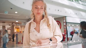 Elegant middle-aged caucasian woman looking glass showcase jewelry and accessories in modern shopping mall. Caucasian blonde woman choosing jewelry in store. Window displays and shoppers background