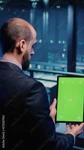 Vertical video: Data center technician holding tablet with green screen in server room, looking at isolated chroma key display. IT engineer inspecting mainframe computer processor, mockup template