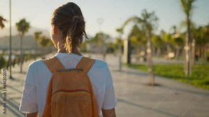 back rear view carefree Woman traveler walking bay sidewalk and watching sunset or sunrise with mountains and sea view. camera following girl