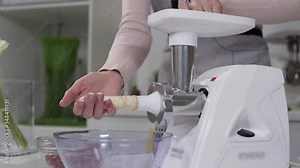 Woman cooks sausages in traditional way using sausage filler of electric mincer machine in kitchen. Production of meat delicacies at home. Preparation of raw beef sausages with electric grinder.