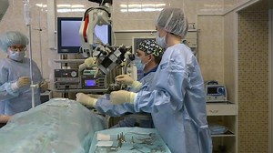 A group of surgeons, a man and two women in a large operating room perform microscopic surgery on ENT organs using a surgical microscope.Innovative technologies in medicine