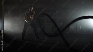 Bodybuilder tirelessly working out with gunex ropes in a darkened gym.