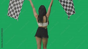 Rear view of brunette waving black and white checkered racing flags to signal start of competition. Young woman posing against background of green screen close up. Slow motion ready, 4K at 59.94fps