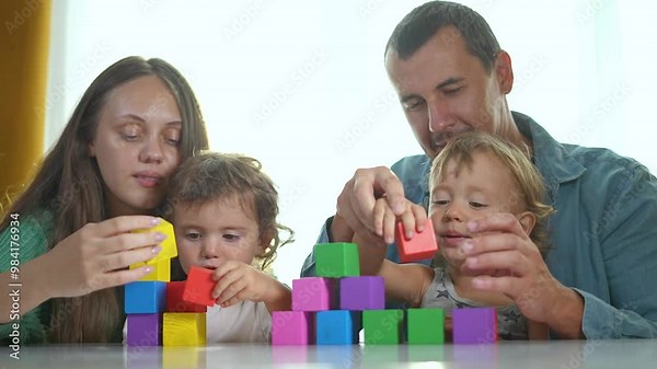 Family playing with colorful constructor cubes at home. Parents helping children build tower with cubes. Family bonding time using constructor. Kids learning and playing with cubes at home. Fun family