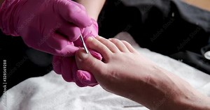 Pedicurist master in pink gloves is cuts the cuticle and shellac toe nails in the pedicure salon using drill. Professional pedicure in cosmetology clinic. Hygiene for feet in beauty salon.