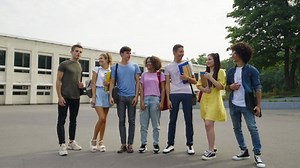 Group of diverse students standing in line against college, laughing and having fun. Cheerful friends posing on campus. Concept of education