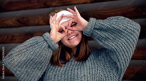 I am batman dude. Portrait of a joyful attractive girl in a sweater and a white hat. Showing I am batman signs with both raised hands and smiling broadly as if taking picture