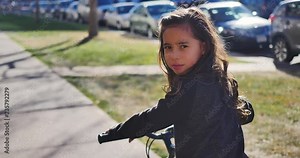 Angry little girl riding bike turns around and says something mean straight to camera