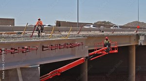 Freeway bridge under lane addition construction with traffic and worker on deck, worker in snorkel lift.