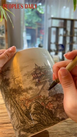 Stroke by stroke, a skilled Chinese artist adorns a porcelain brush pot with impeccably detailed paintings, showcasing extraordinary craftsmanship. | People's Daily, China