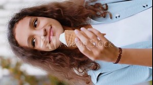 Happy pretty preteen child kid standing and eating ice cream in waffle cup. Cute smiling tween girl enjoys yummy ice cream licking, relaxing on summer holidays in urban european city street. Vertical