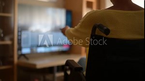 Woman In A Wheelchair Changing Channels On The Television With A Remote Control. Representation Of How Technology Facilitates Inclusion In Daily Activities.Inclusion In Home Entertainment. Streaming.