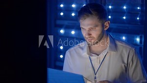 Male Server Engineer in Data Center. IT engineer inspecting a secure server cabinet using modern technology laptop coworking in data center.