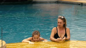 The mother with little daughter have fun in the pool. Mom plays with the child. The family enjoy summer vacation in a swimming pool jumping, spinning, splash water. Slow motion.