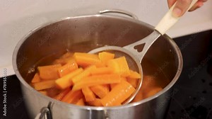 Boiling carrots in a pot, carrots boiling in boiling water, lifting boiled carrots with a ladle